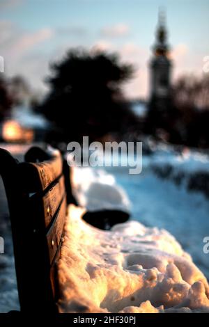 Woden benches lit by the evening sun. Snow in the park.Selective focus. Stock Photo