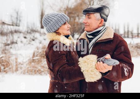 Senior family couple dancing outdoors during snowy winter weather. Elderly people having fun walking. Valentine's day Stock Photo