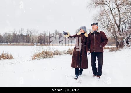 Senior family couple walking outdoors during snowy winter weather. Elderly people holding hands enjoying landscape. Valentine's day Stock Photo