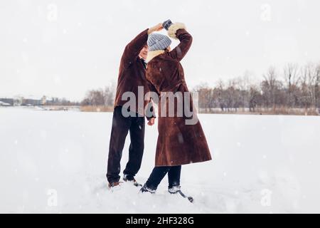 Senior family couple dancing outdoors during snowy winter weather. Elderly people having fun. Valentine's day walk Stock Photo