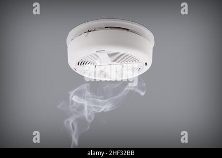 Smoke detector installed on a ceiling with rising smoke underneath Stock Photo