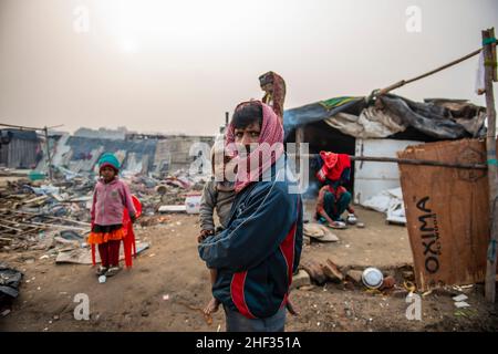 Ghaziabad, India. 13th Jan, 2022. A man seen holding his child standing near cluster of slums.Poor people living in urban slum area of vasundhara, Urban poverty in India is now over 25 percent, close to 81 million people in urban areas live below the poverty line. Several reports indicate that the national level of around 150-199 additional million people will become poor due to COVID-19 crisis, while those who are already poor will be pushed deeper into poverty. (Photo by Pradeep Gaur/SOPA Images/Sipa USA) Credit: Sipa USA/Alamy Live News Stock Photo