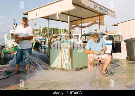 Two fisherman who are twin brothers mending their nets after a fishing trip at first light in the small French fishing port of Sanary sur Mer, Cote d' Azur in the south of France. 2014. Stock Photo