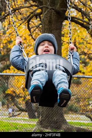 Two year old boy swinging on city park swing set; Corinthian Gardens; Philadelphia; Pennsylvania; USA Stock Photo