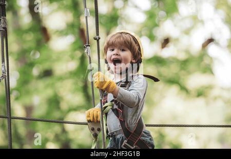 Cargo net climbing and hanging log. Portrait of a beautiful kid on a rope park among trees. Rope park - climbing center. Safe Climbing extreme sport Stock Photo