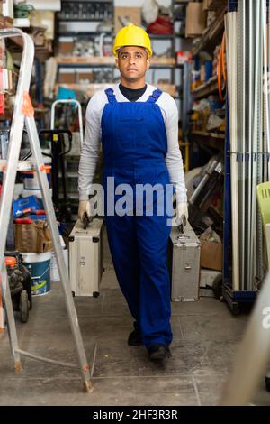 Portrait of worker in protective helmet and overalls with toolbox in hardware store Stock Photo