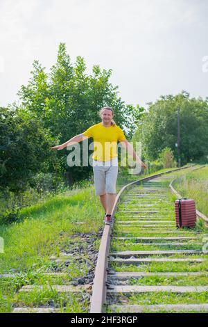 long-haired traveler with a red suitcase walks along the rails Stock Photo