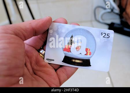 A Christmas themed $25 Amazon gift card with seasonal holiday decorations: a snow globe, snow flakes, tree, and wrapped presents; e-commerce. Stock Photo