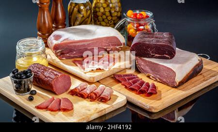 An assorted spread of delicatessen cure meats including parma ham, salamis, aged beef and pastrami on wooden cutting boards Stock Photo
