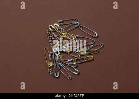 Dark-brown background with tiny silver and gold safety pins scattered chaotically in center. Copy space. Mock up photography. Creative minimalism with Stock Photo