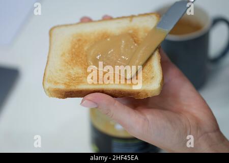 Hand smears peanut butter on crispy toast, close-up Stock Photo