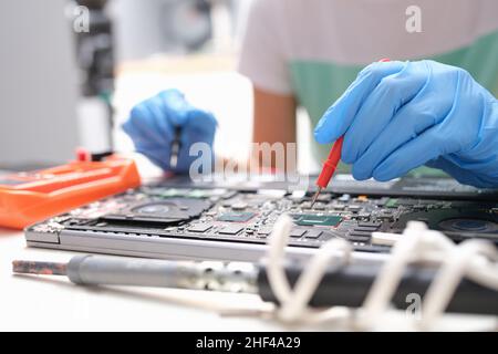 Repairman hands hold screwdrivers over laptop microcircuit, close-up, blurry. Replacing parts, upgrading an electronic device Stock Photo