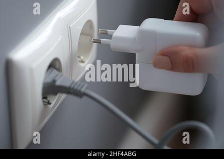 Female fingers plug the adapter into an outlet, close-up. White socket on gray wall background, electrician in apartment Stock Photo