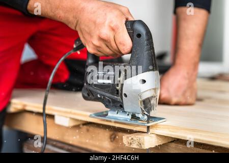 Close up on hand of unknown carpenter working with an electric jigsaw cutting wood with saw woodworking hobby concept Stock Photo