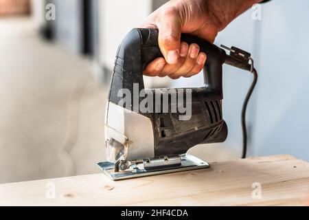 Close up on hand of unknown carpenter working with an electric jigsaw cutting wood with saw woodworking hobby concept Stock Photo