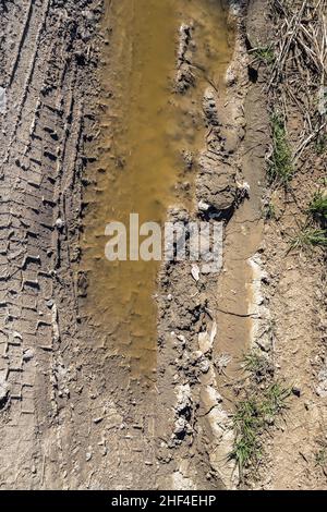 Tire tracks on a muddy road in the countryside. Puddles in the pits of a country dirt road. Stock Photo