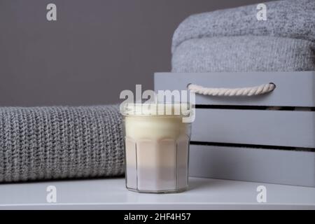 homemade scented multicoloured beige candle in mason jar with gray knit sweaters in a wooden box. Handmade craft organic gift. Monochrome product adve Stock Photo