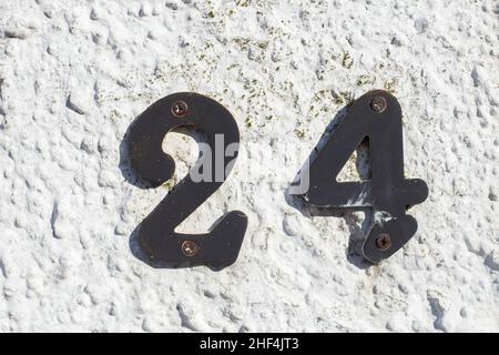 A old iron number 24 on a rough white wall, post office. Stock Photo