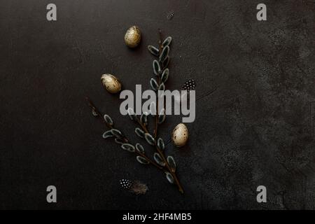 Happy Easter concept. Preparation for holiday. Golden decorated easter eggs willow feather on trendy grunge scratched dark black shale background. Simple minimalism flat lay top view copy space Stock Photo