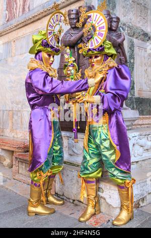 Two participants in colourful historic Venetian fancy dress costumes pose at Four Tetrarchs Statue, Venice Carnival, Carnevale di Venezia, Italy Stock Photo