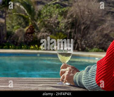 Hands holding a glass of white wine by the swimming pool. Focus in front. Stock Image. Stock Photo