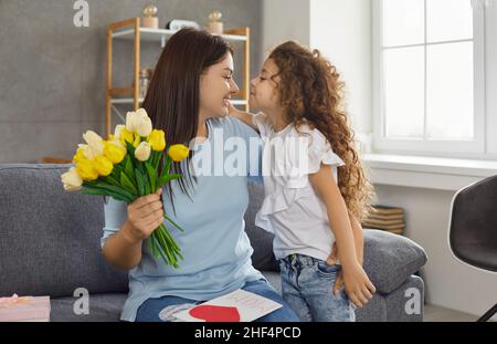 Happy mom kisses little daughter and thanks her for presents and flowers for Mother's Day Stock Photo
