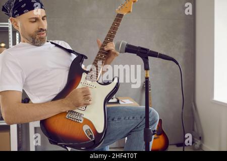 Male guitarist playing riff on his electric guitar in modern studio with microphone Stock Photo