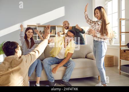 Two cheerful multiracial men give high five to each other while having fun at home with friends. Stock Photo