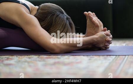 Woman Practices Yoga Asanas in Morning for Energy for the Whole Day. Yoga Lady Doing Seated Forward Bend Exercise Face Down.Close-up. Stock Photo