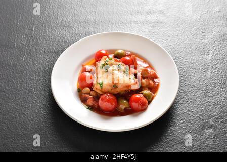 Cod stew with chickpeas, cherry tomatoes and olives on plate over dark stone background. Close up view Stock Photo