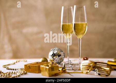 Champagne flutes with gold colored decoration and gift boxes against beige backdrop, copy space Stock Photo