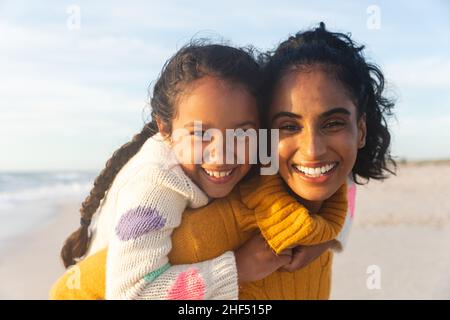 Portrait of happy biracial woman giving piggyback ride to daughter at sunset Stock Photo