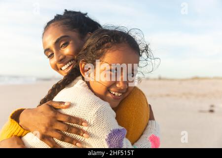 Portrait of smiling biracial mother and daughter embracing each other at beach during sunset Stock Photo