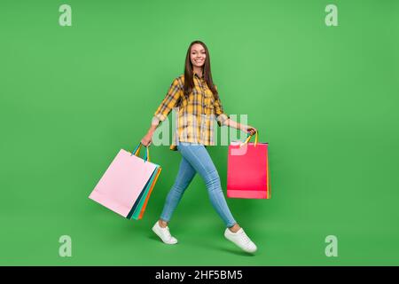 Full size profile portrait of cheerful positive girl hold packages walking isolated on green color background Stock Photo