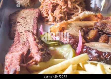 american barbecue tray with porchetta, pulled pork, coleslaw salad, brisket, barbecue sauce, pulled pork dumpling, french fries, selective focus Stock Photo