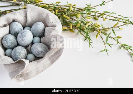 In a basket with a linen napkin on a white background are marble-colored Easter eggs and willow twigs. Easter greeting card with place for text. Horiz Stock Photo