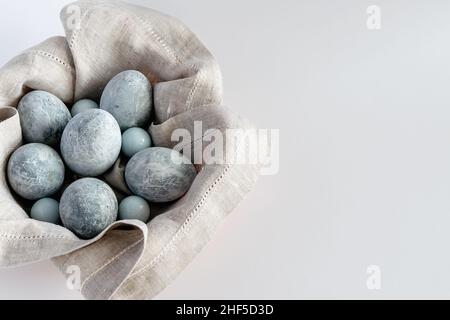 Marble-colored Easter eggs in a basket with a linen napkin on a white background. Easter greeting card with place for text. Horizontal photo. Stock Photo