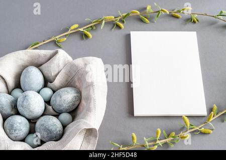 On a gray background in a basket with a linen napkin are marble-colored Easter eggs and willow twigs and an empty notebook. Horizontal photo. Stock Photo