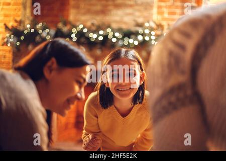 Happy parents with kids enjoying Christmas time at home. Father, mother and children near fireplace decorated with xmas lights, family toasting marshm Stock Photo