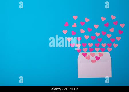 Overhead view of pink hearts coming out from white envelope on blue background, copy space Stock Photo