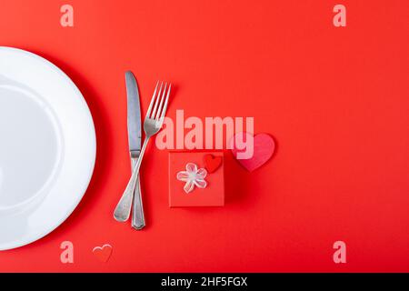 Overhead view of place setting by gift and heart shaped decoration on red background, copy space Stock Photo