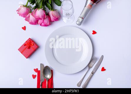 Overhead view of fresh pink roses and place setting with gift over white background, copy space Stock Photo