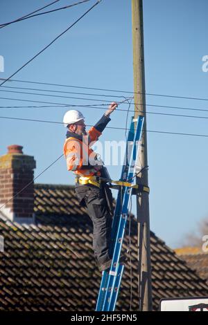 Open reach telecommunications engineer at work up a ladder, he is ...