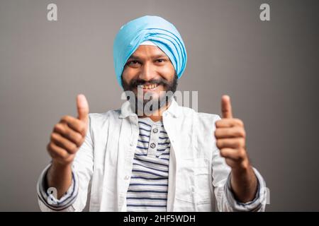 happy Young indian sikh man showing thumbs up hand gesture by looking at camerea - Concept of self-confident, positive emotion and successful people. Stock Photo