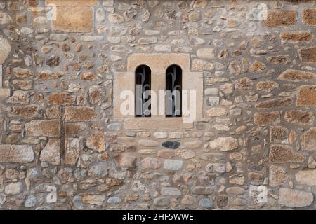 Old stone wall with a double arched window and metal grating Stock Photo