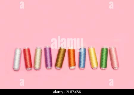 Colored thread spools on a pink background in a top view Stock Photo