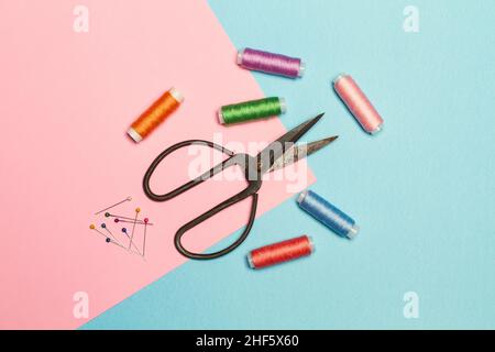 Colored thread spools and sewing accessories on a pink and light blue background in a top view Stock Photo