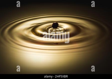Black drop falls into the water and creates circles Stock Photo