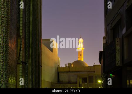 Illuminated minaret of Grand Mosque in Dubai (Grand Bur Dubai Masjid) at night, seen in between the buildings of Bur Dubai, United Arab Emirates. Stock Photo