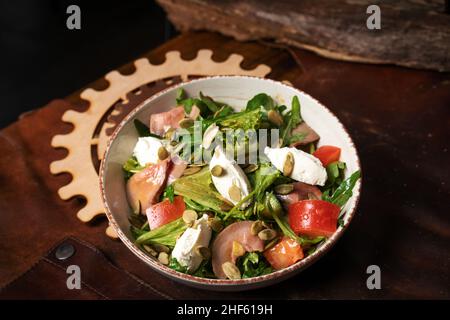 Fresh Vegan Salad with Vegetables, Fish, Cheese, Egg, Pumpkin Seeds, Arugula in White Ceramic Bowl on a Leather Apron. Top view. High quality photo Stock Photo